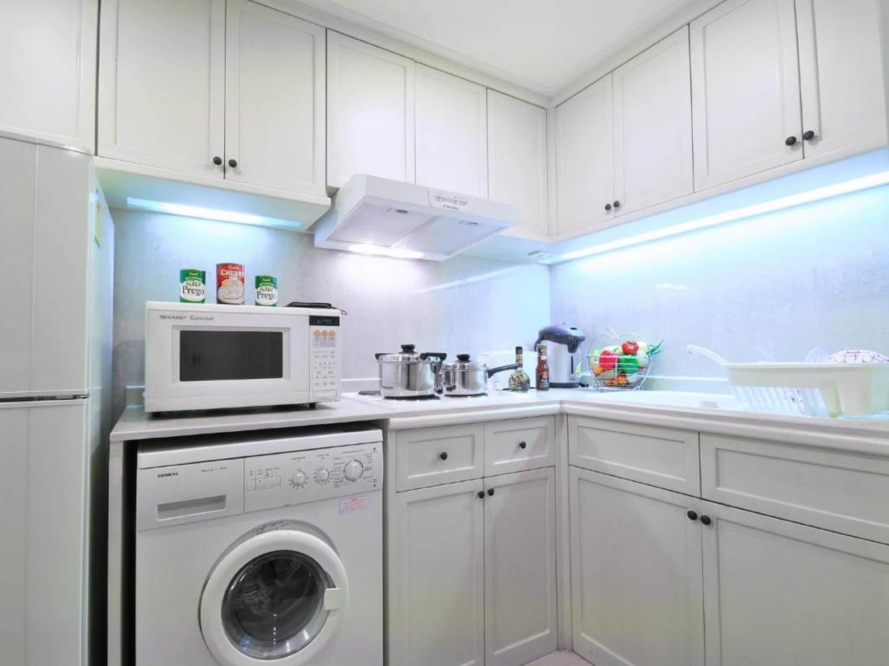 A compact kitchen with white cabinets, a microwave, a washing machine, and a stove.