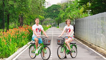 Two people on bicycles on a paved path with greenery on both sides.