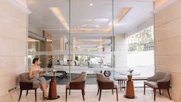 A modern lobby with a glass partition, a woman seated at a table, and a view of the street outside.