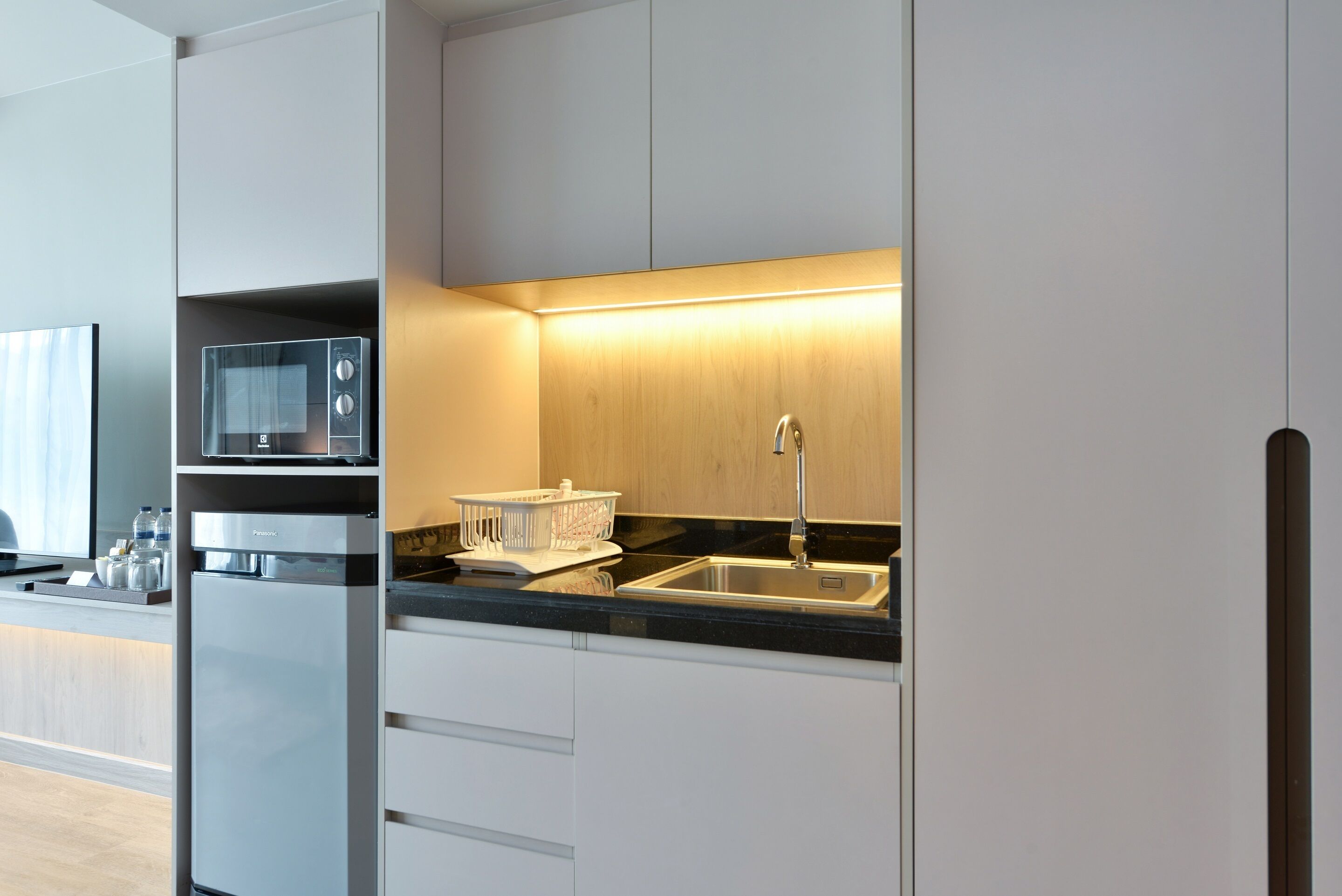 A modern kitchen with a built-in microwave, a sink, and a wooden cabinet.