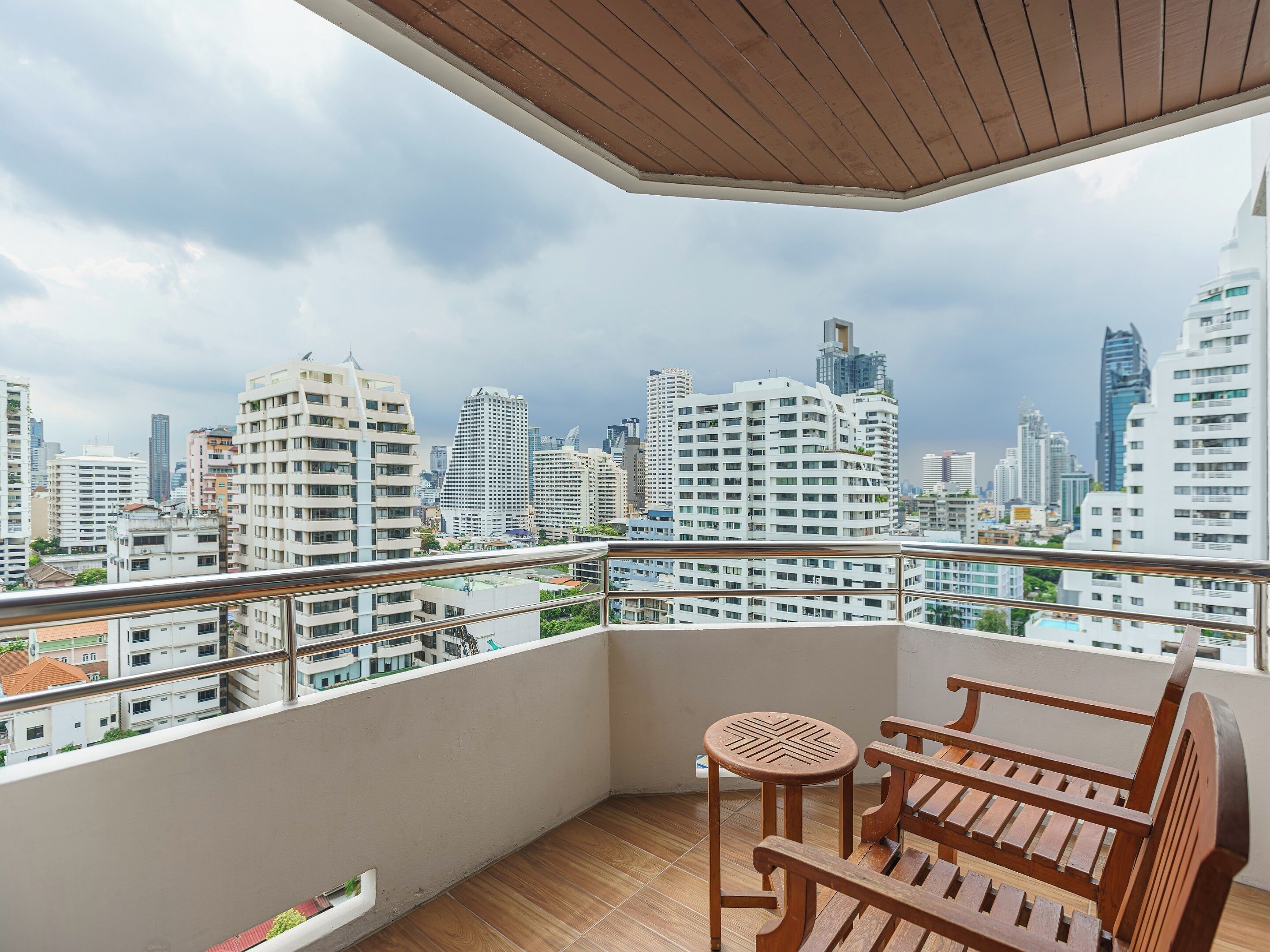 A balcony with a wooden bench and a small table, overlooking a cityscape with modern buildings.