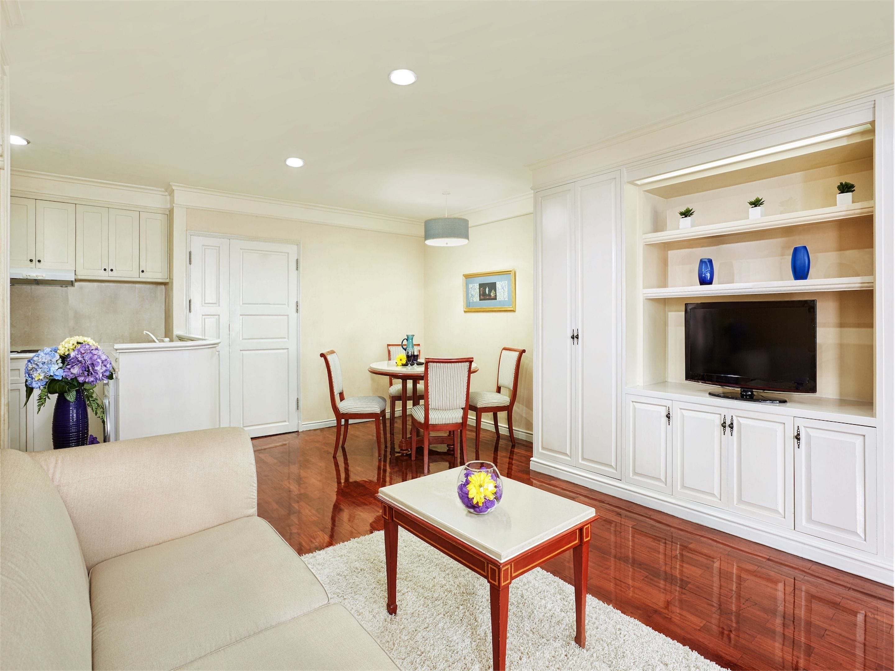 Una sala de estar con sofá, una mesa de centro, un comedor con sillas, una cocina con armarios y un televisor sobre un mueble.