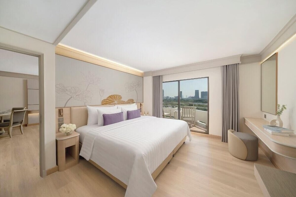 A modern hotel room with a large bed, a desk, and a balcony with a city view.