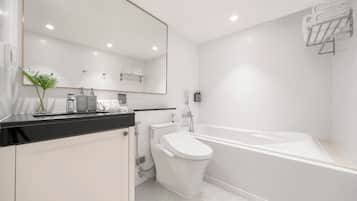 A modern bathroom with a white toilet, a bathtub, a large mirror, and a black countertop with toiletries.