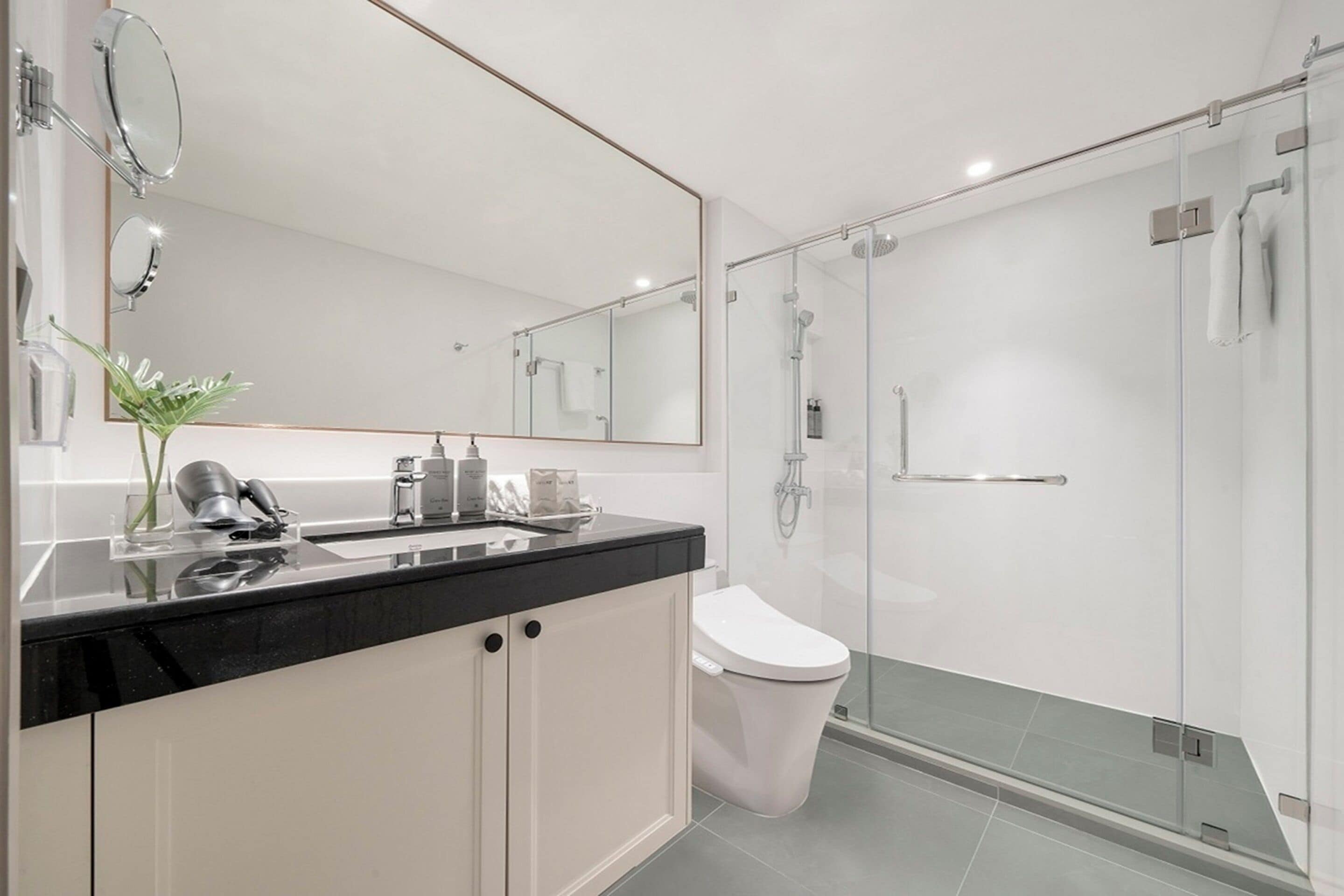 A modern bathroom with a black countertop, white cabinets, a large mirror, and a glass-enclosed shower.
