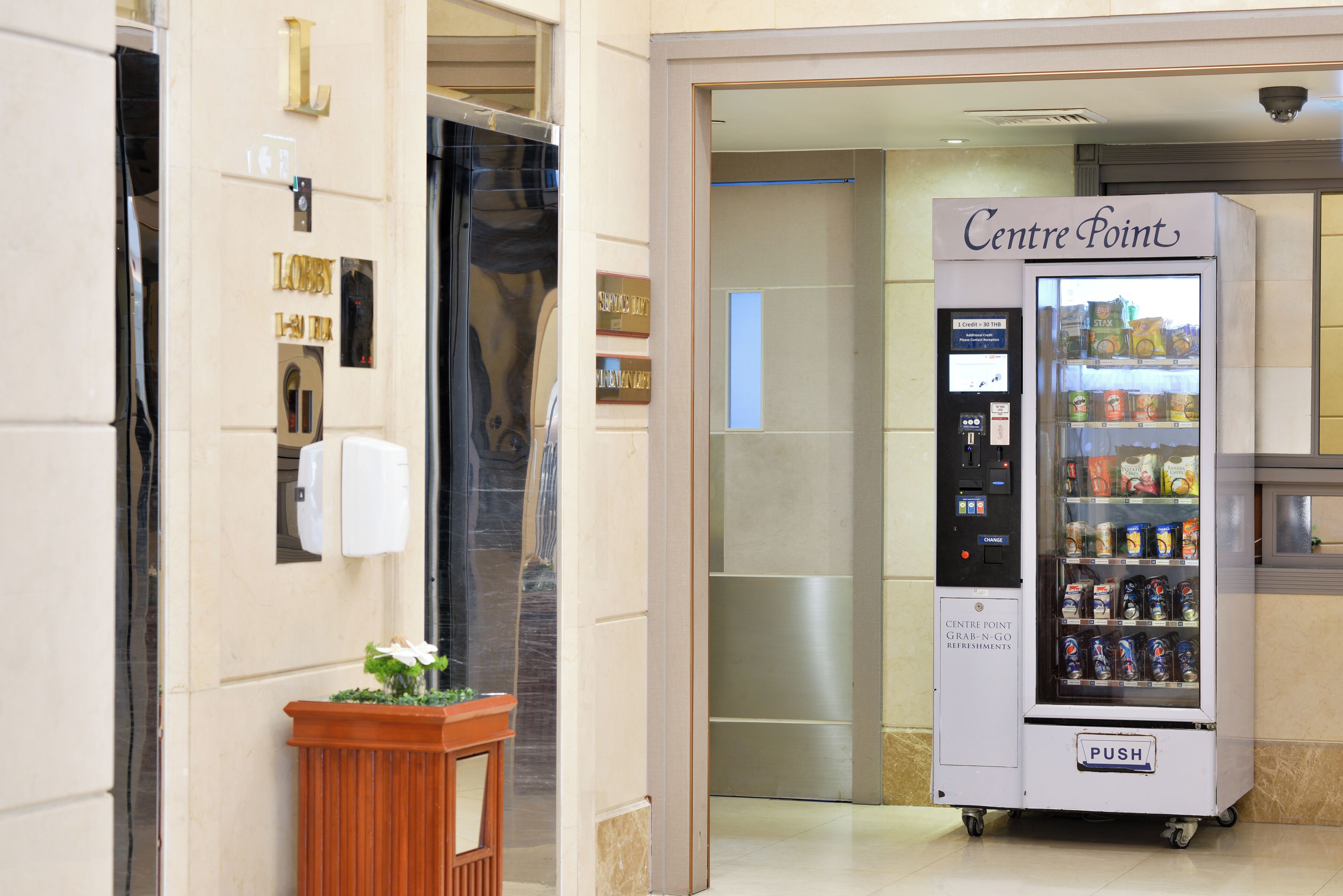 A vending machine labeled "Centre Point" in a hallway with a potted plant and a door with a mirror.