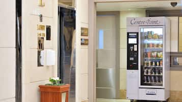 A vending machine labeled "Centre Point" in a hallway with a potted plant and a door with a mirror.
