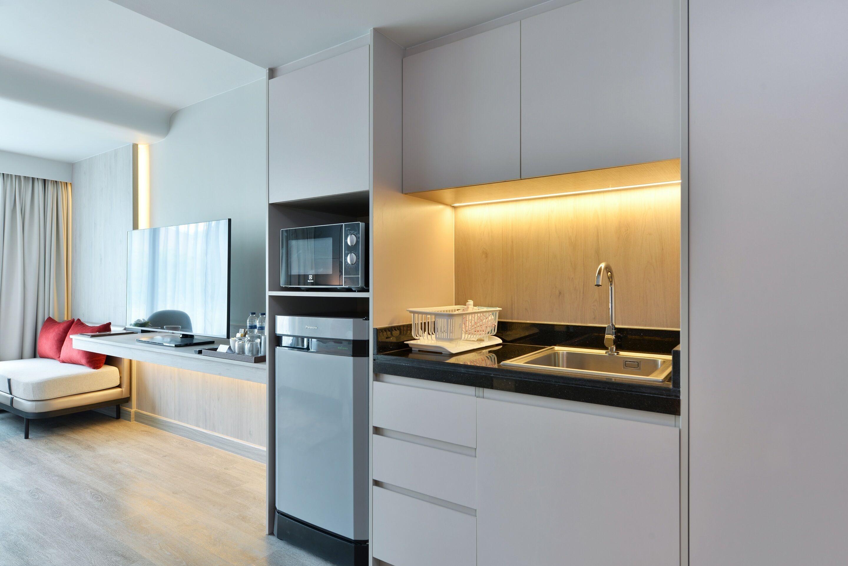 Una cocina moderna con microondas, horno y lavaplatos integrados. Cuenta con una pequeña zona de comedor con mesa y sillas.