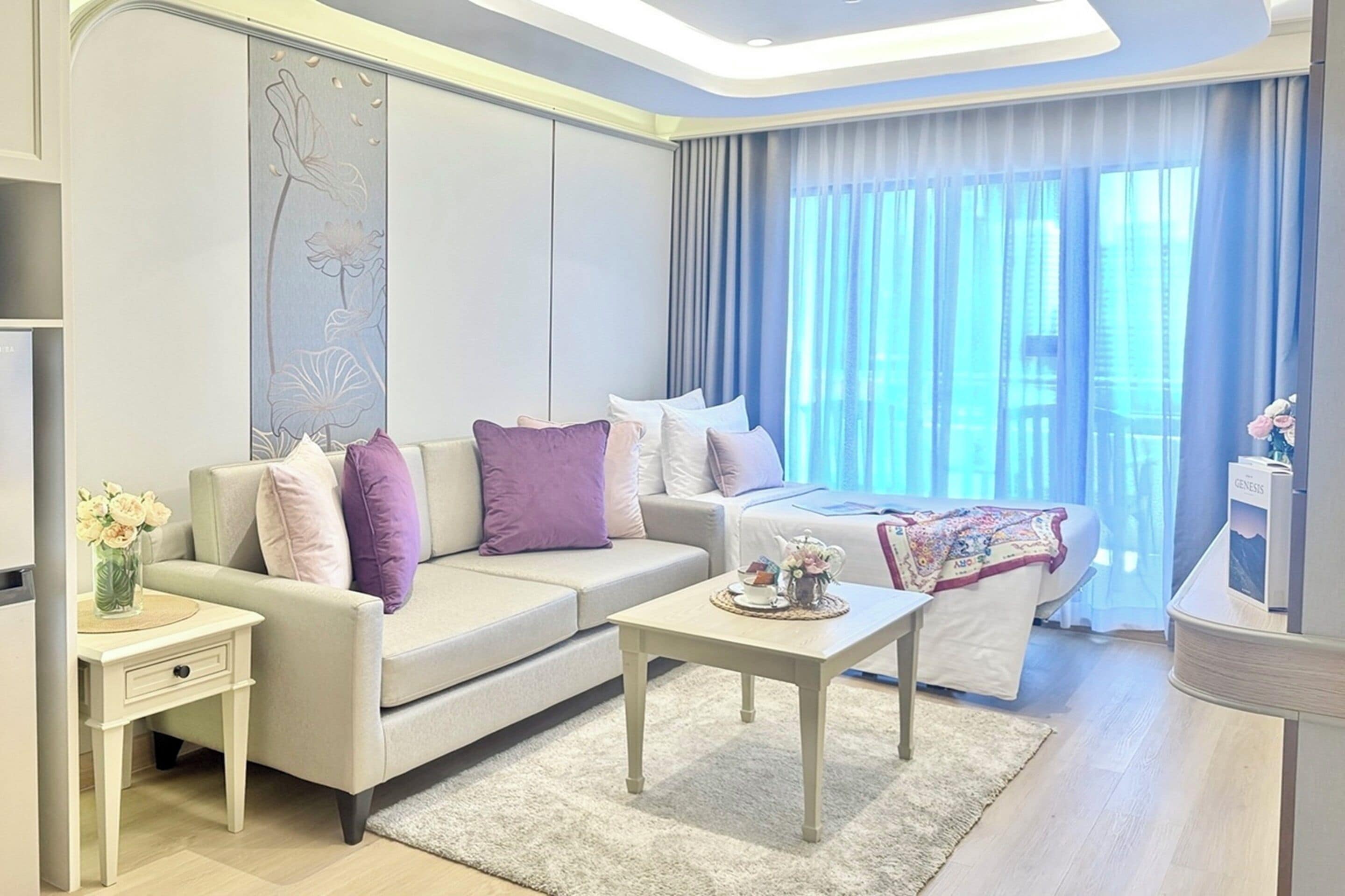 A modern hotel room with a sofa, a bed, a small table, and a nightstand.