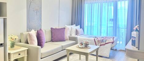 A modern hotel room with a sofa, a bed, a small table, and a nightstand.