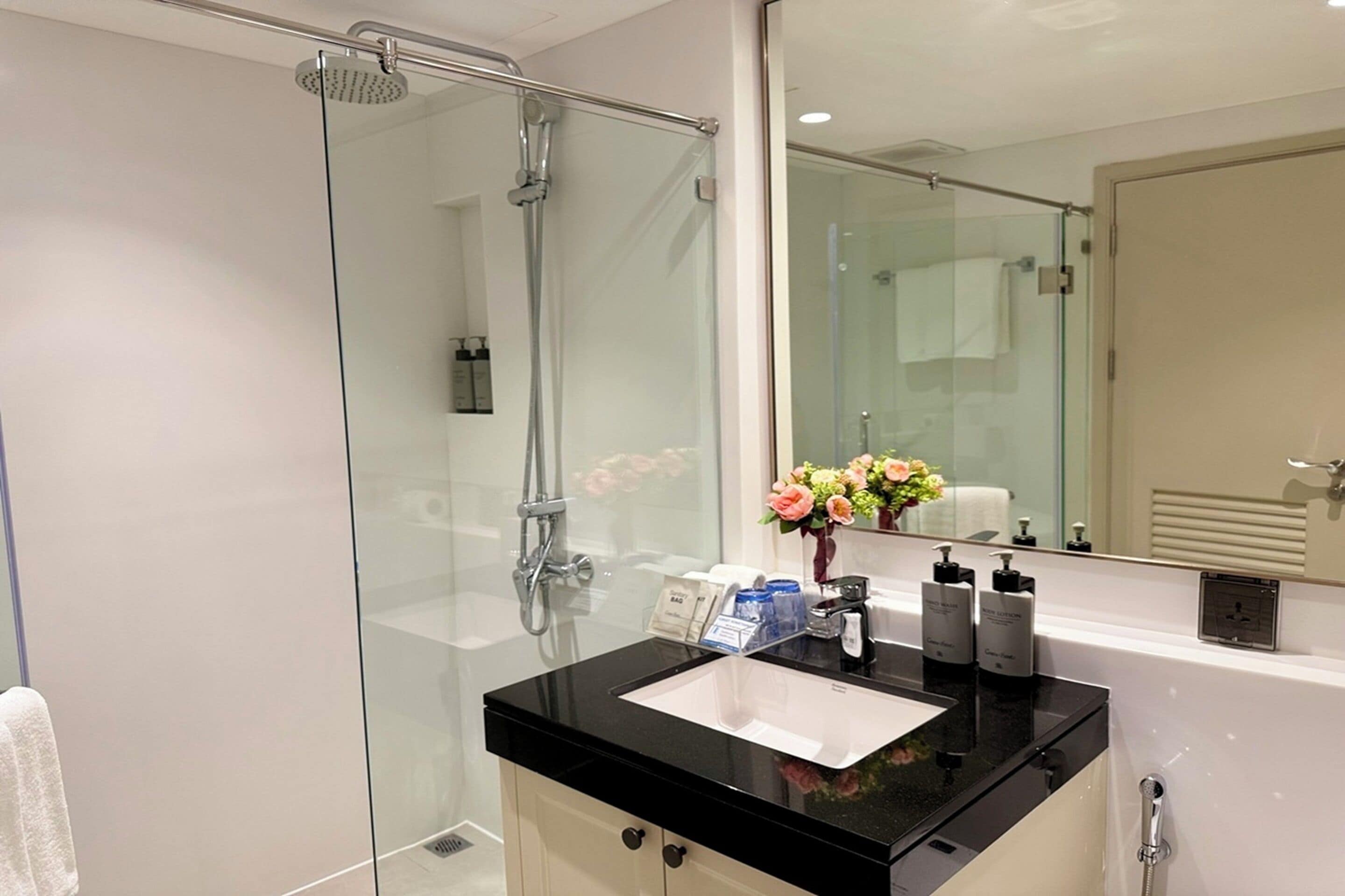 Un baño moderno con cabina de ducha de vidrio, lavamanos con encimera negra y un espejo grande.