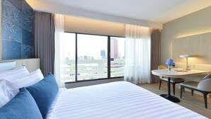 A hotel room with a large bed, a round table, and a view of the cityscape through the window. - Centre Point Plus Hotel Pratunam (Bangkok)