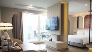 A hotel room with a bed, a desk with a lamp, a TV mounted on the wall, and a balcony with chairs. - Centre Point Plus Hotel Pratunam (Bangkok)