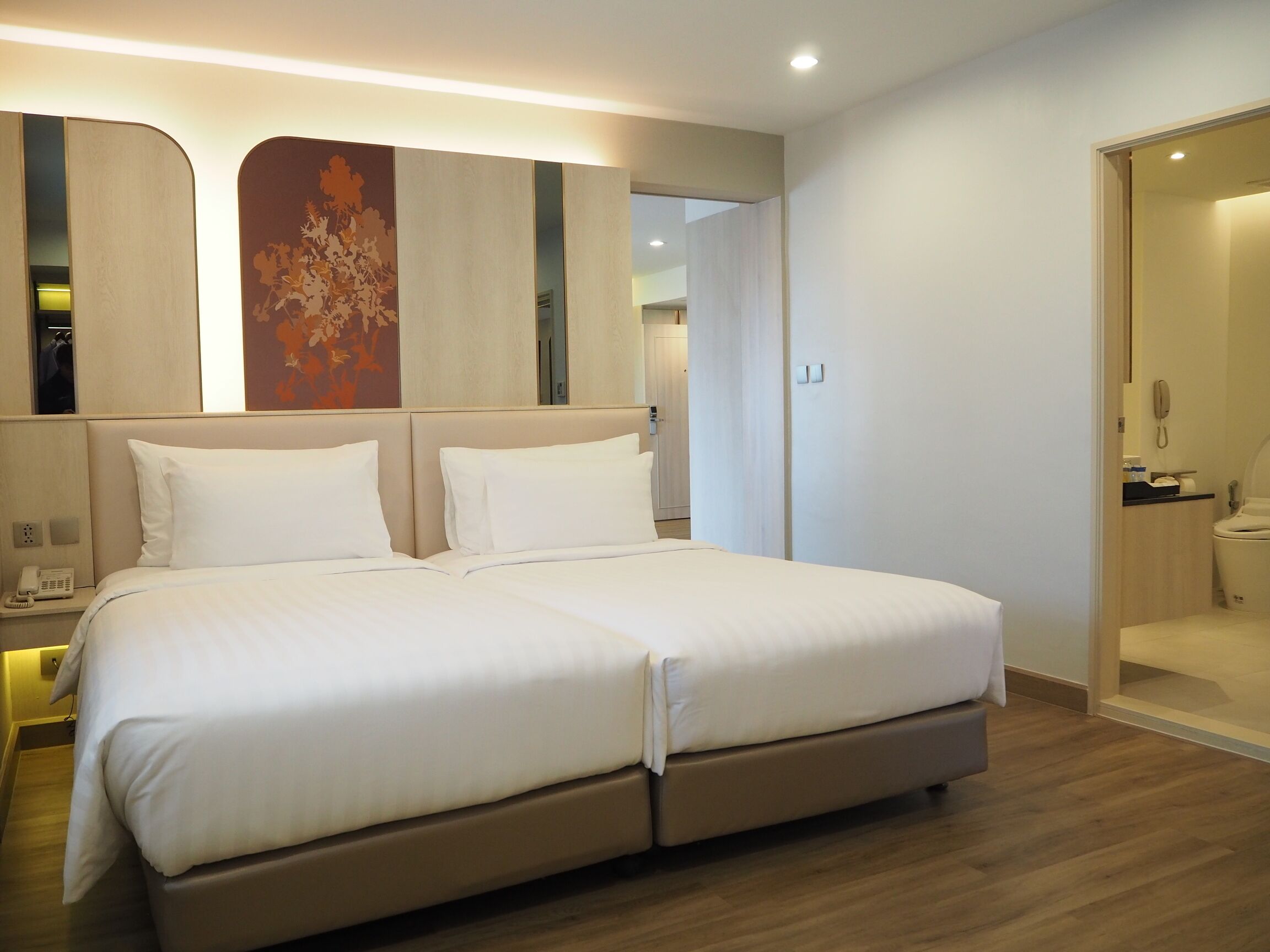 Une chambre d’hôtel moderne avec un grand lit, un téléphone sur la table de chevet et une salle de bain visible à travers une porte ouverte.