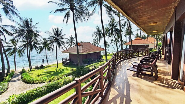 Un complexe hôtelier doté d’une terrasse en bois offrant une vue sur une plage, des palmiers et l’océan.