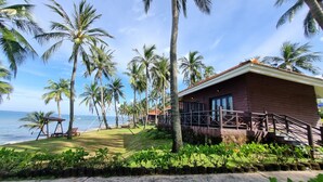 Une propriété située en bord de mer, avec un bâtiment en bois, des palmiers et une vue sur l’océan.