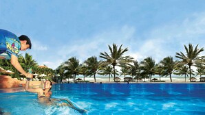 Une piscine à l’eau d’un bleu cristallin, entourée de palmiers et avec une plage en arrière-plan.