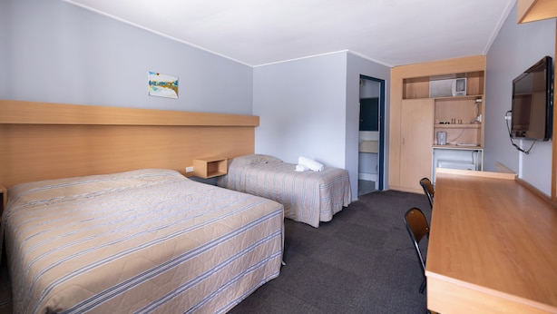 A hotel room with two beds, a desk, a chair, a television, and a kitchenette. - Windsor Heritage Motel (Windsor)
