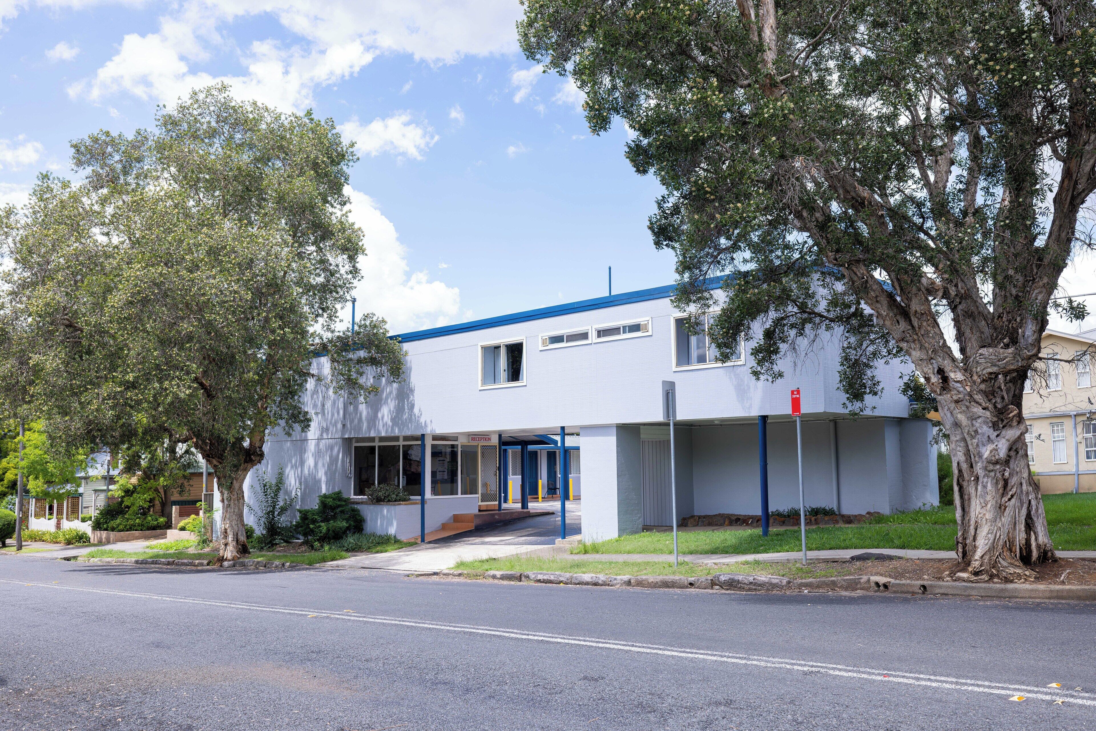 A modern building with a blue roof, a covered entrance, and a large tree in front.