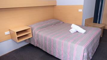 A single bed with a striped bedspread, a wooden headboard, a small shelf, and a door to the right.