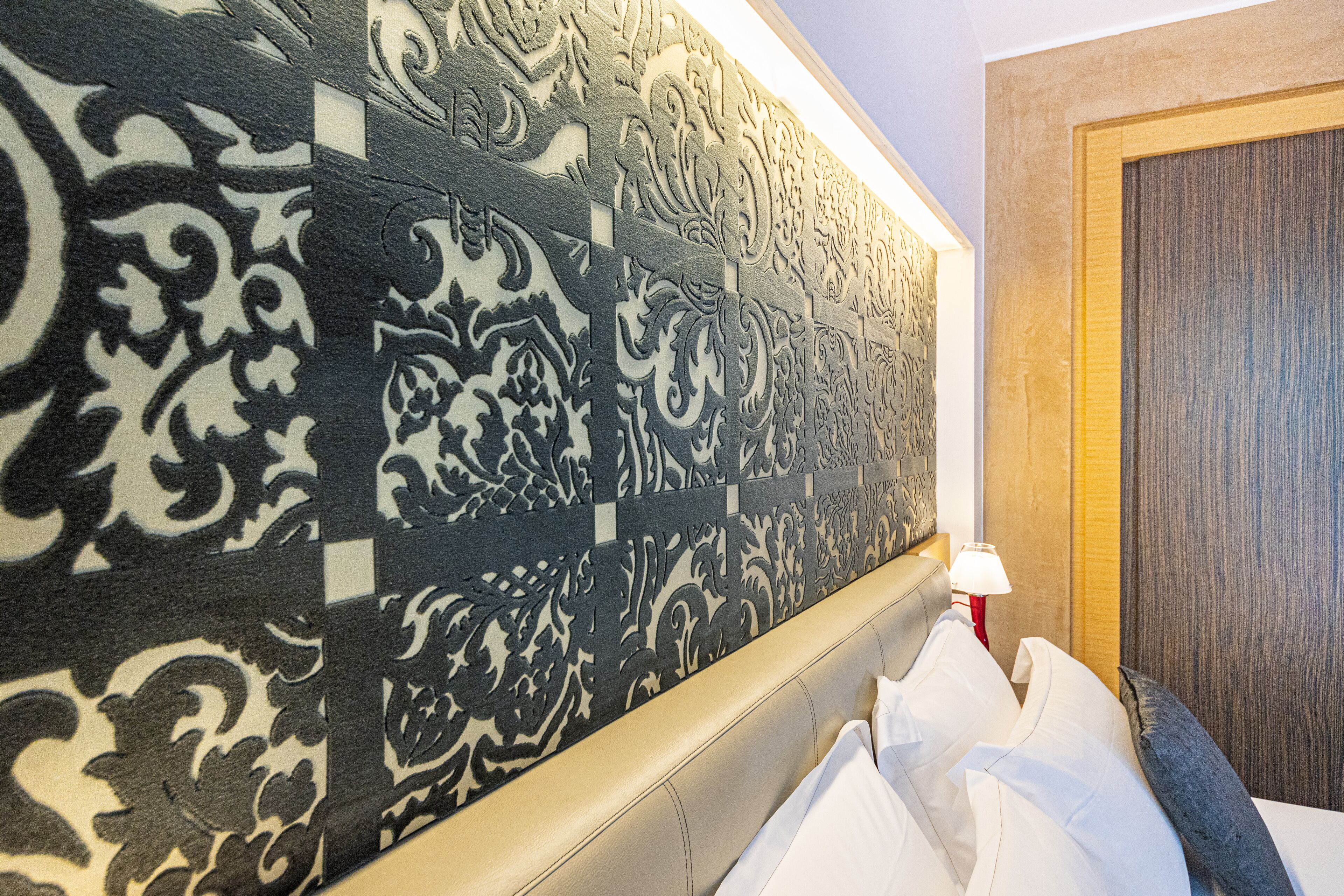 A hotel room with a decorative headboard, a wooden door, and a bedside lamp.