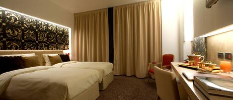 A hotel room with two beds, a desk with a chair, a dining table with a tray of food and drinks, and a large window with curtains.