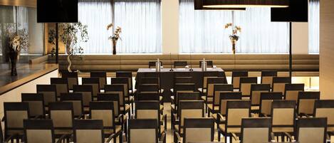 A conference room with rows of chairs, a long table, and large windows with curtains.