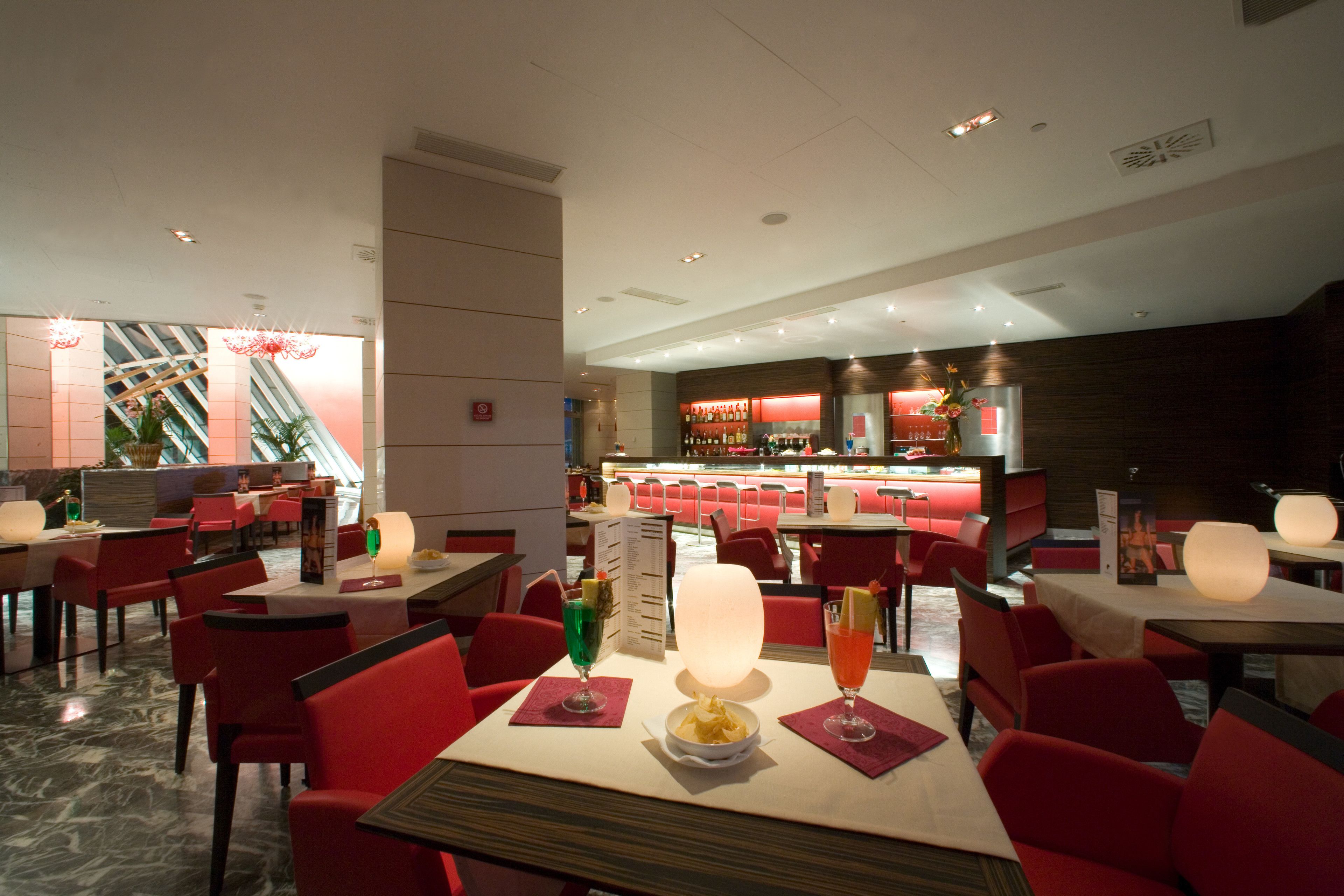 Un restaurante con sillas y mesas rojas, una zona de bar y una escalera al fondo.