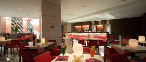 Un restaurante con sillas y mesas rojas, una zona de bar y una escalera al fondo.