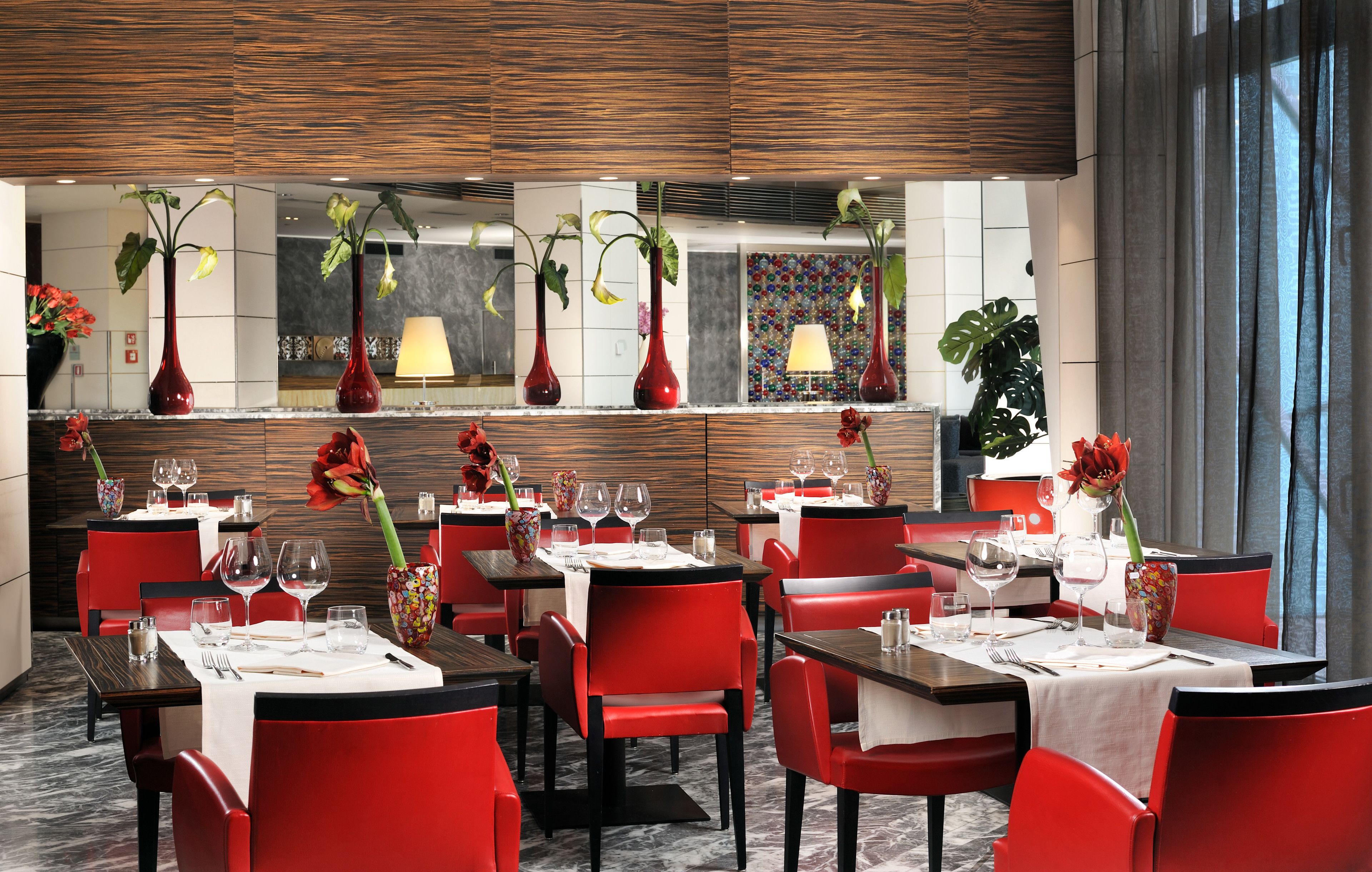 Ein Restaurant mit roten Stühlen und Tischen, an jedem Tisch Weingläser und Besteck.
