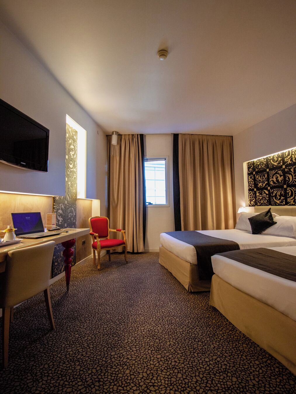 A hotel room with a bed, a desk with a laptop, a chair, and a TV.