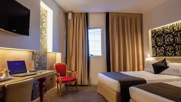 A hotel room with a bed, a desk with a laptop, a chair, and a TV.