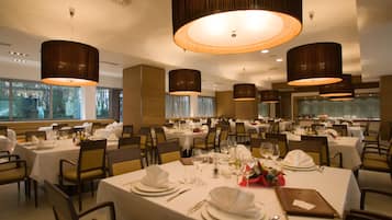 Un restaurant doté de nombreuses tables dressées pour le service, avec des nappes blanches, des couverts disposés avec soin et un éclairage d’ambiance.