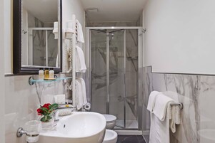 A bathroom with a glass shower enclosure, a sink with a vase of flowers, and a mirror with a towel rack.