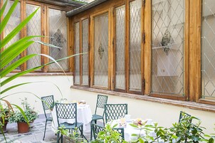 A patio with wooden-framed windows, green chairs, and potted plants.