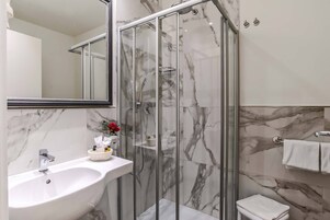 A modern bathroom with a marble sink, a glass-enclosed shower, and a white toilet.
