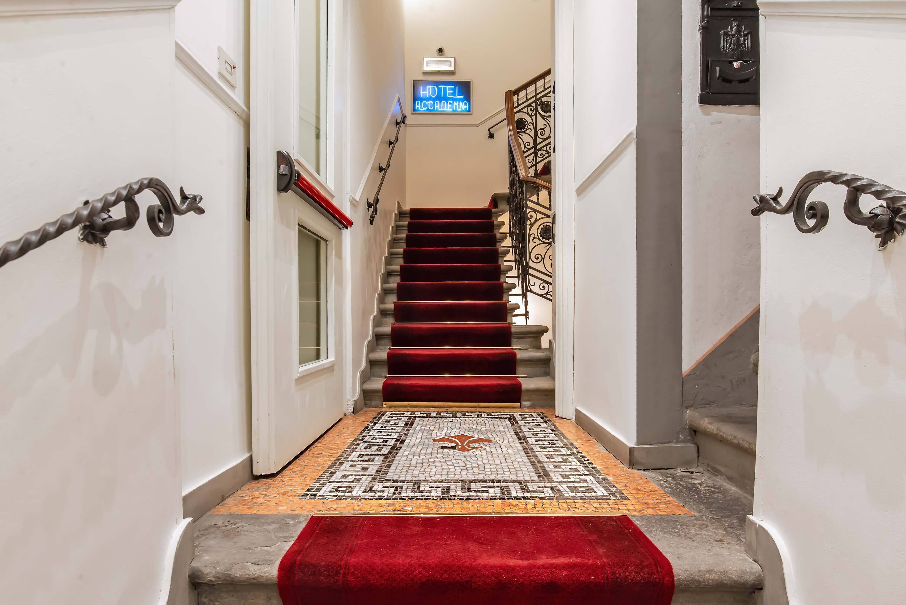 A hotel staircase with a red carpet, a patterned rug, and a sign indicating the hotel's name.