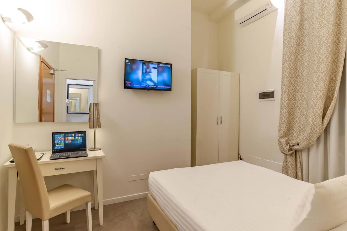 A hotel room with a bed, a desk with a laptop, a TV mounted on the wall, and a wardrobe.