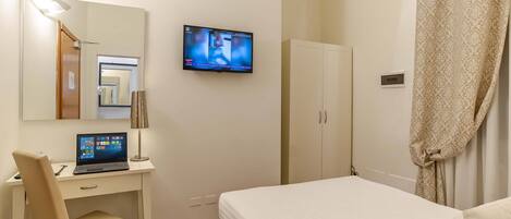 A hotel room with a bed, a desk with a laptop, a TV mounted on the wall, and a wardrobe.