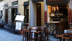 A street view with outdoor seating at a restaurant, a bicycle parked in front, and a building with a wine sign.