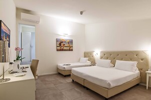 Quarto de hotel com duas camas, uma escrivaninha com luminária, um quadro na parede e um aparelho de ar condicionado.