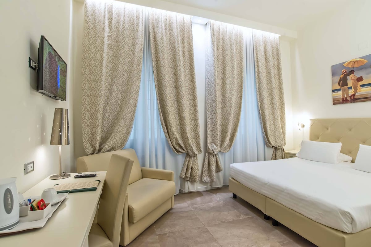 A hotel room with a bed, a sofa, a TV mounted on the wall, and a painting on the wall.