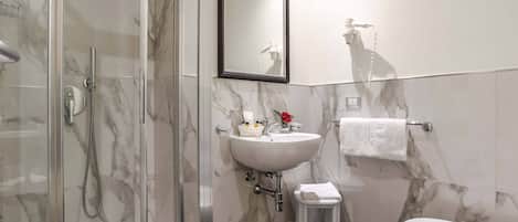 Ein Badezimmer mit einer gläsernen Duschkabine, einem weißen Waschbecken mit Spiegel darüber, einer Toilette und einem Handtuchhalter.