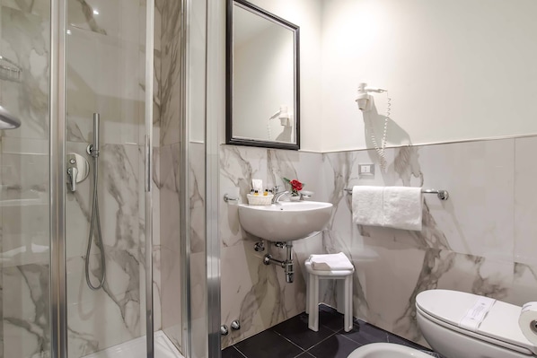 A bathroom with a glass-enclosed shower, a white sink with a mirror above it, a toilet, and a towel rack.