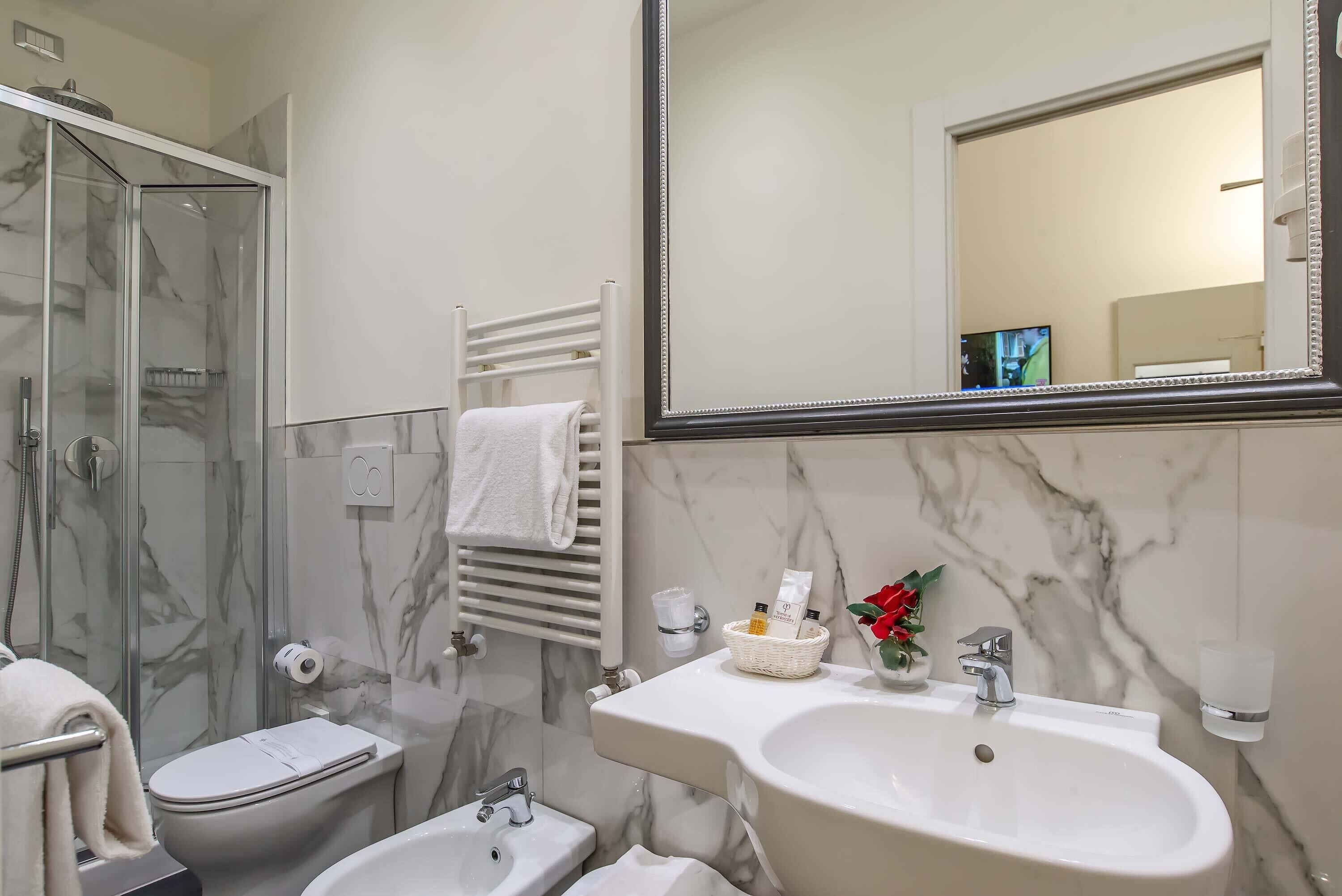 Un baño moderno con ducha de vidrio, inodoro, bidé y lavamanos con resalte de mármol.