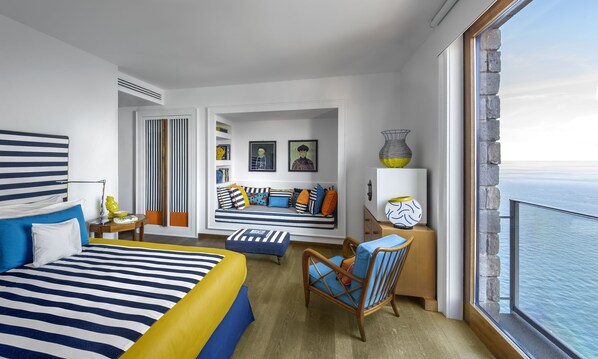 Una habitación de hotel moderna con una cama grande, un sofá, un sillón y vistas al mar.