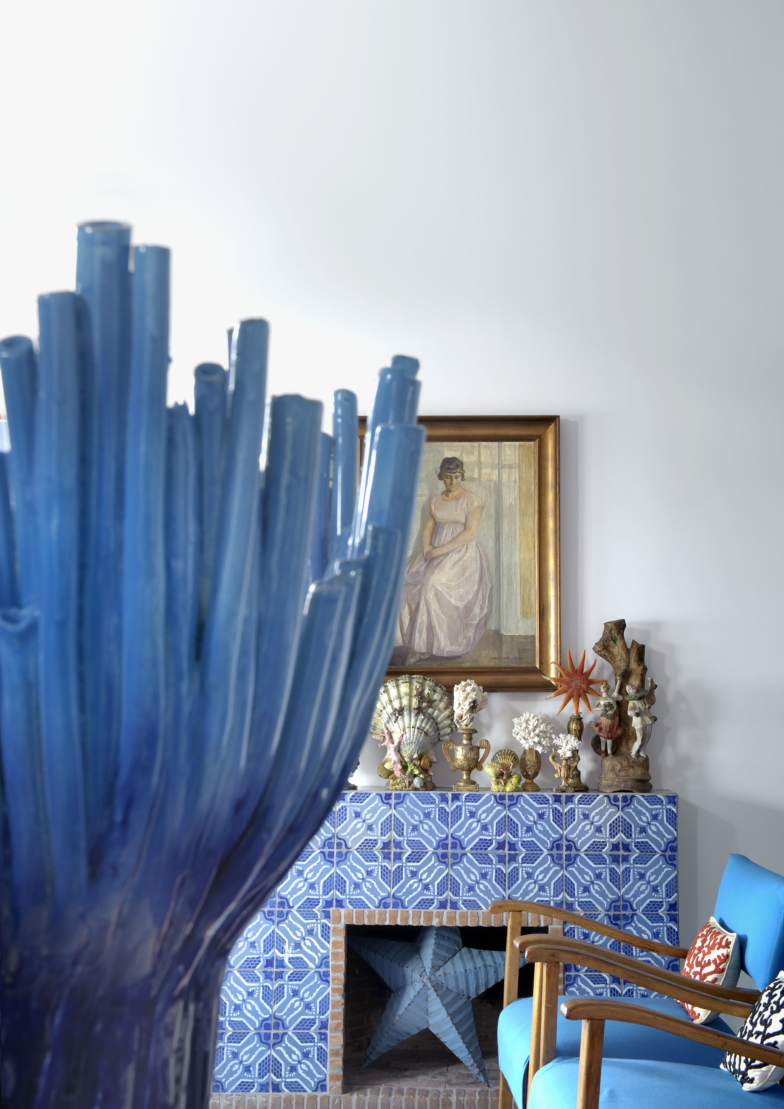 A room with a blue patterned fireplace, a framed painting, and a blue chair.