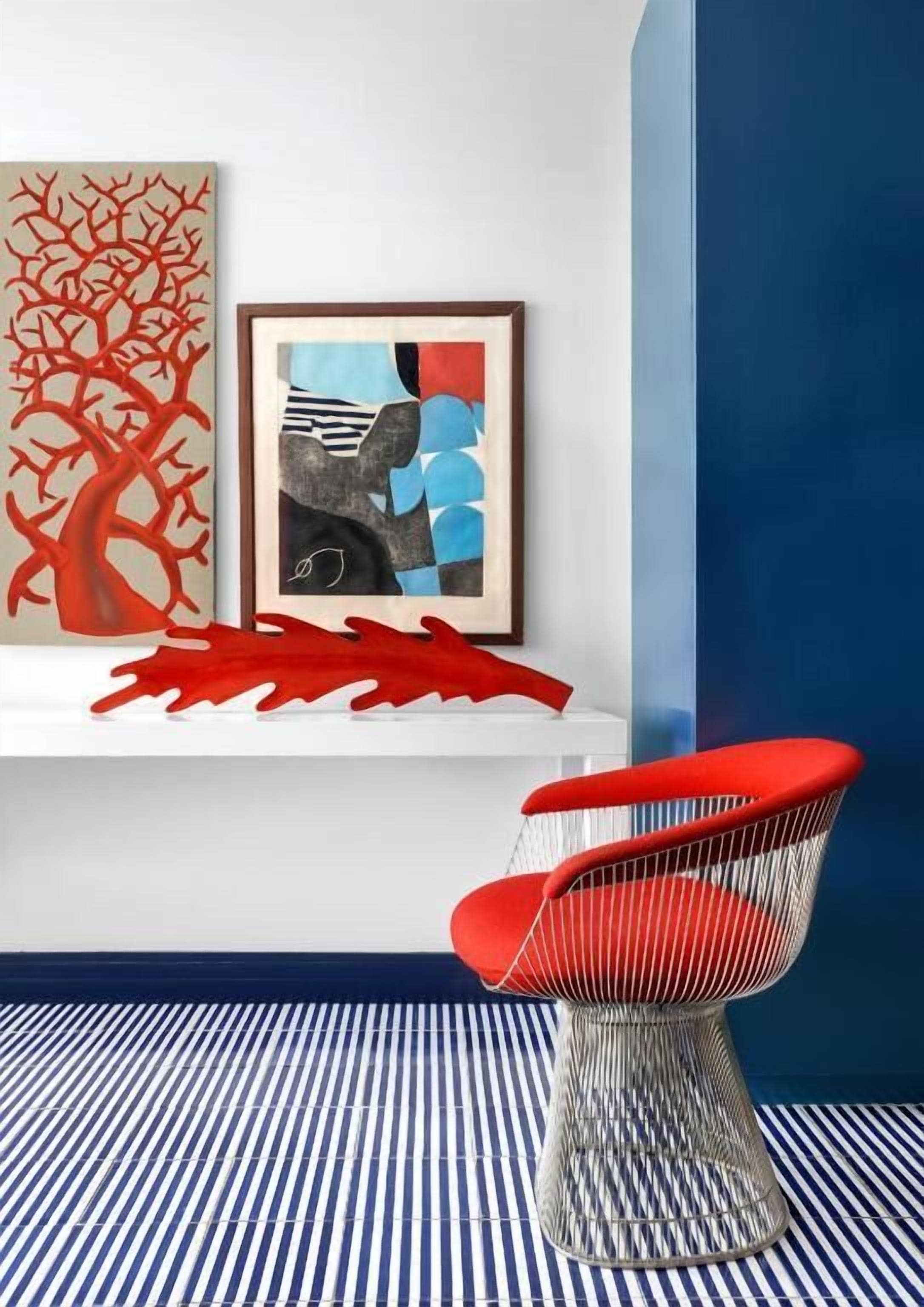 A modern room with a red chair, a white shelf with artwork, and a striped floor.