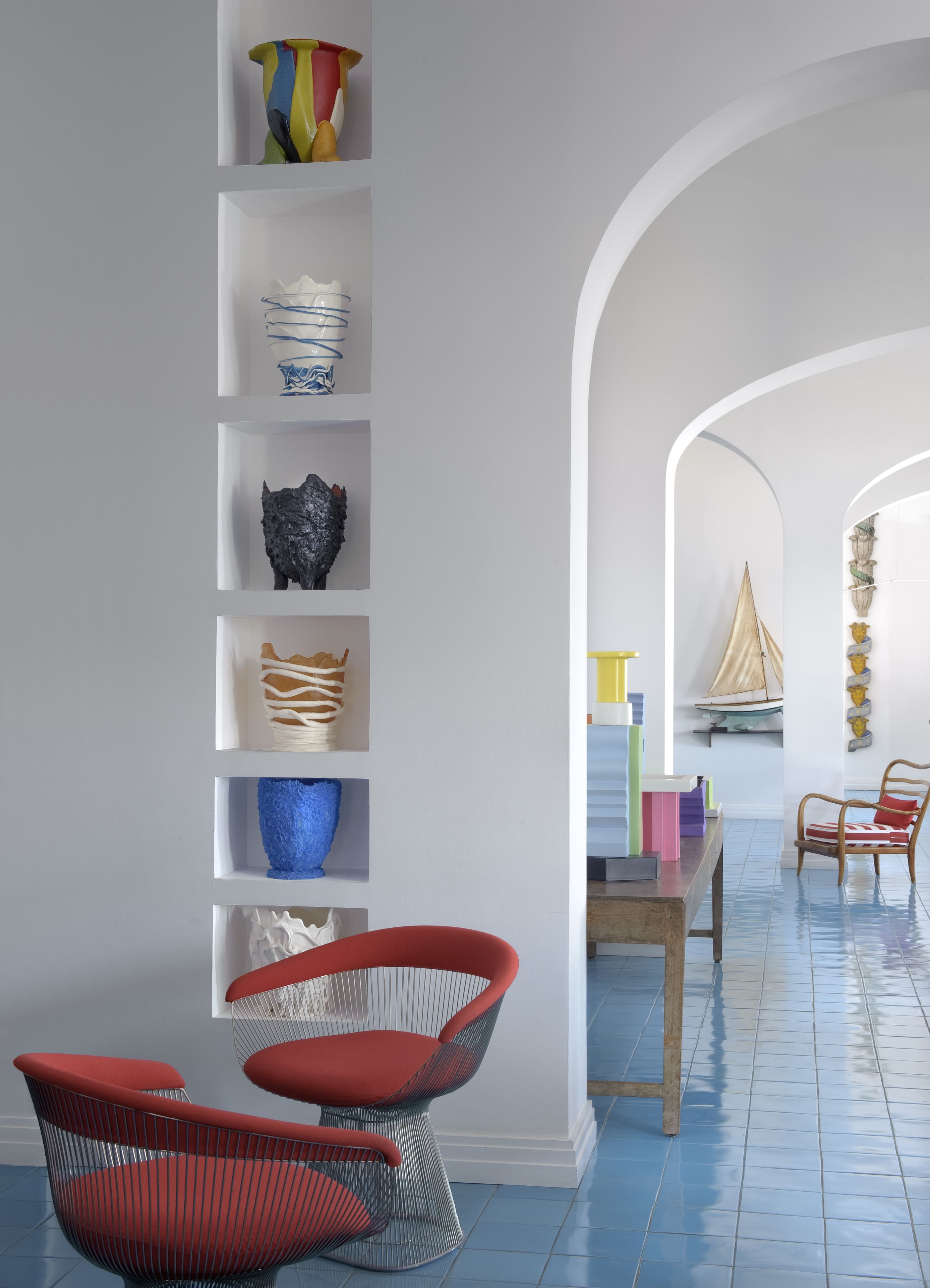 A modern interior with a white wall, shelves with various decorative items, a wooden table with chairs, and a tiled floor.