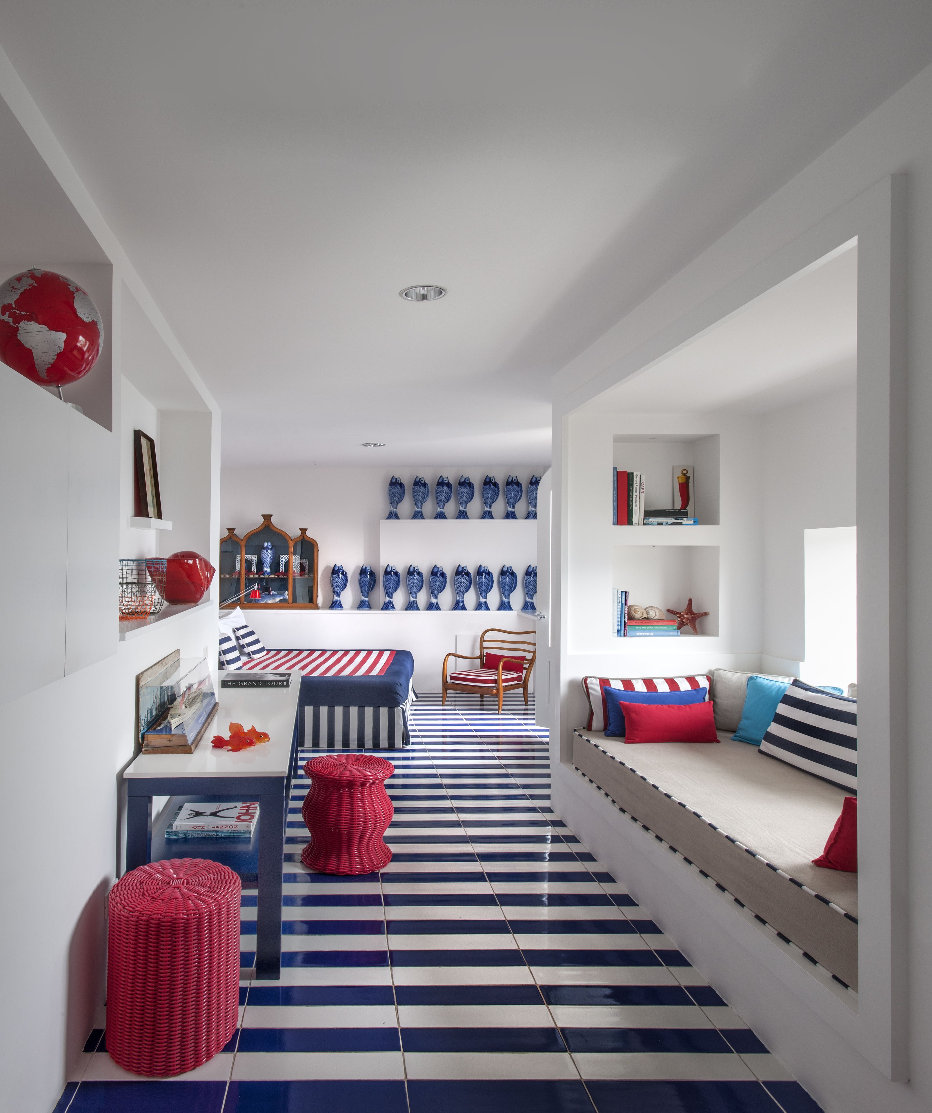 Une pièce moderne et bien éclairée, avec un sol à rayures, une table à rayures bleues et blanches, un tabouret tissé rouge, une chaise en bois et un canapé avec des coussins à rayures.
